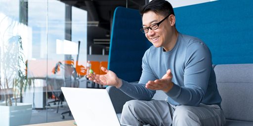 Young man smiling and expressing happiness while looking at his open laptop.