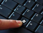 Finger pressing the Windows key on a computer keyboard.